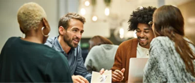 En grupp med fyra personer som sitter vid ett bord och deltar i en diskussion. Två håller i en tidsskrift och en har en bärbar dator.