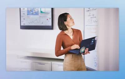 Person holding a laptop in an office with a whiteboard in the background.