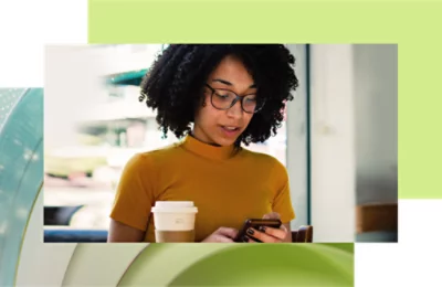 Seorang wanita dengan atasan kuning dan kacamata menggunakan smartphone sambil memegang cangkir kopi dalam latar kafe.