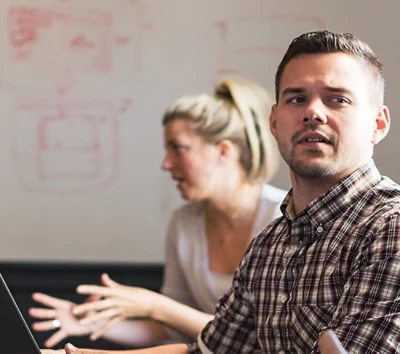 A man and woman sitting at a table looking at a laptop.