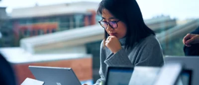 A woman in a green top focused on her laptop screen, partially framed by a blue graphic element