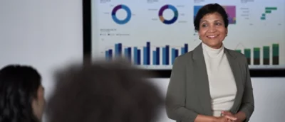 Osoba w garniturze stojąca przed ekranem, na którym wyświetlona jest litera C.