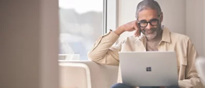 Laptop na stole, przy którym siedzi osoba.