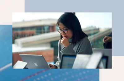 Person working on a laptop in an indoor setting with other devices visible in the foreground.