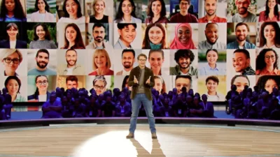 En person står vid ett podium, i bakgrunden visas flera bilder en skärm.