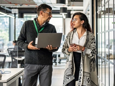 Due professionisti che discutono, uno con un portatile e l'altro uno smartphone, in un ambiente di ufficio moderno.