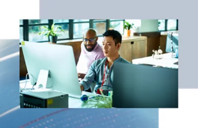 Due colleghi seduti a una scrivania, che lavorano insieme su grandi monitor desktop in ufficio.