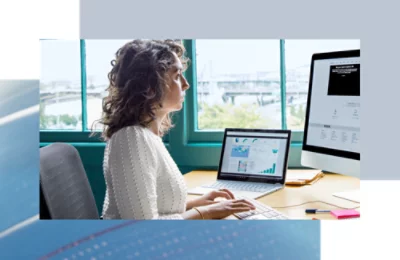 Persona che lavora a una scrivania, visualizzando grafici e dati su due schermi di computer.