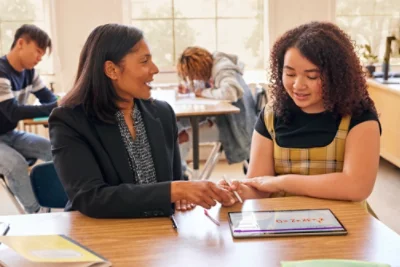 A woman and a girl are seated at a table, engaged with a tablet, sharing a moment of learning.