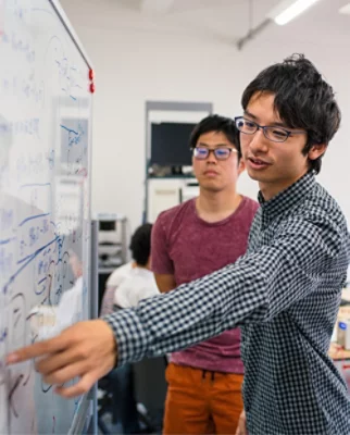 En man i en rutig skjorta som pekar på en whiteboard.