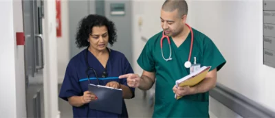 A man and woman in scrubs, holding a folder and a clipboard respectively.
