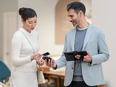 En man med en surfplatta och en kvinna med ett smartphone som ler och engagerar sig på ett kontor, båda i professionell affärsklädsel.