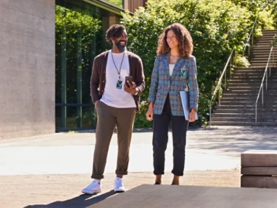 En man och en kvinna står utomhus, kvinnan bär rutig jacka och mannen håller i en telefon.