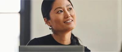 En person med långt mörkt hår och ringörhängen, i en väl upplyst inomhusmiljö, tittar uppåt med ett leende.