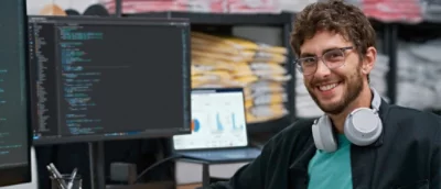 En man med hörlurar ler och har en skärm bredvid sig