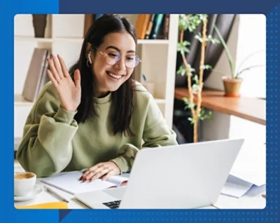 Eine Frau winkt einem Laptop zu, in dessen Nähe eine Topfpflanze steht.