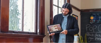 Ein Mann hält ein Tablet in der Nähe eines Fensters mit Blick auf Bäume.