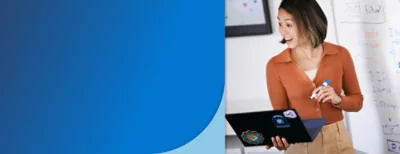 En person, som står framför en whiteboard med anteckningar, håller i en bärbar dator och en filtpenna.