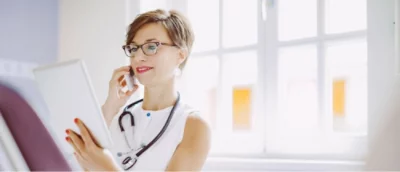 En kvinna med kort hår och glasögon talar i mobiltelefon.