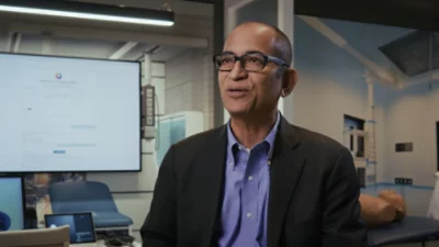 Business professional standing in a laboratory setting with a monitor displaying a web interface.