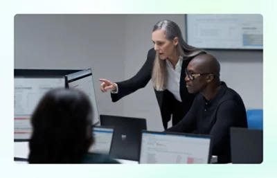 Two people looking and pointing at desktop monitors with graphs on them