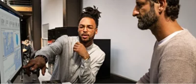 Zwei Männer, die auf den Bildschirm blicken und sich unterhalten.