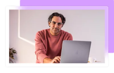 Ένας άντρας που φοράει γυαλιά και ένα ροζ μπλουζάκι κάθεται μπροστά από έναν φορητό υπολογιστή.