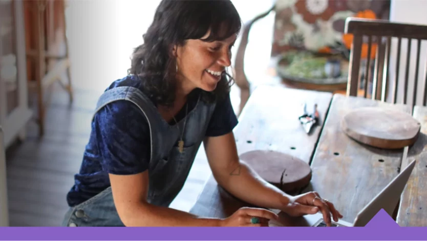 A casually-dressed woman works on a laptop at home.