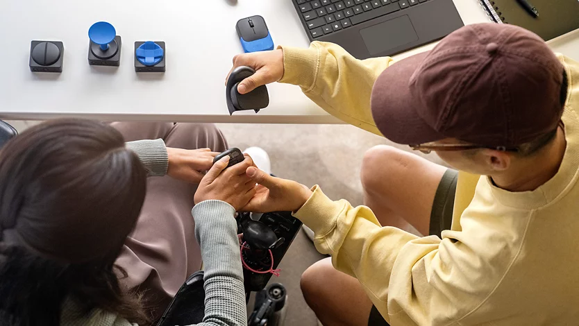 Osoba na wózku inwalidzkim pokazuje współpracownikowi, jak skonfigurować Akcesoria adapatacyjne Microsoft.