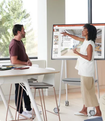 A person giving a PowerPoint presentation to a colleague in an open office.