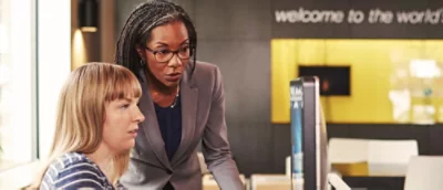 Seorang wanita berambut panjang yang mengenakan kacamata berdiri di dalam ruangan dengan teks selamat datang di dunia terlihat.