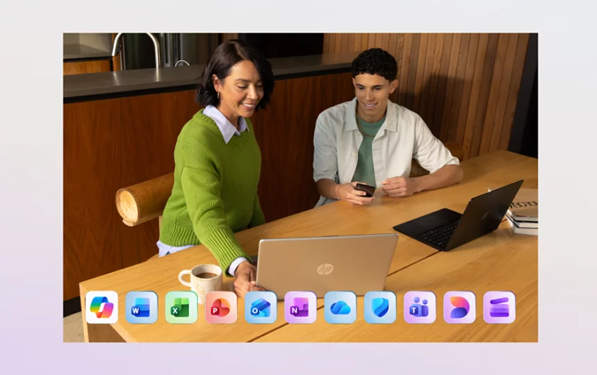 Dos personas utilizan dos portátiles en una mesa de comedor en los que aparece una fila de aplicaciones de Microsoft 365 en la parte inferior, como: Microsoft Copilot, Word, Excel, PowerPoint, Outlook, OneNote, OneDrive, Microsoft Defender, Microsoft Teams, Microsoft Designer y Clipchamp.