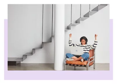 A person sitting in a leather chair with a laptop on their lap and their arms raised