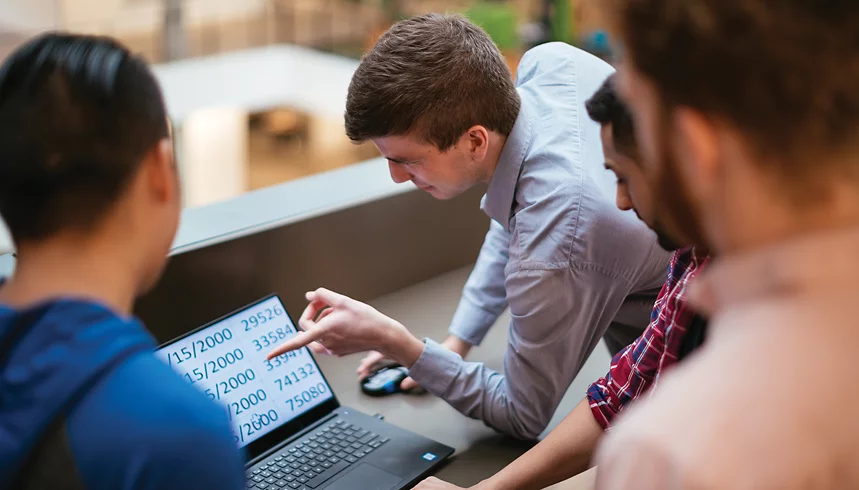 A person who has low vision points to a laptop screen while talking to co-workers. 
