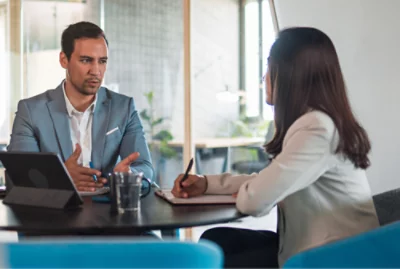 A professional man and woman discussing work at a table with a laptop and water pitcher 