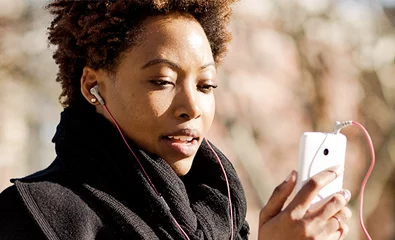 Uma pessoa ao ar livre, vestida a rigor com um cachecol e um casaco pretos, a olhar para um smartphone. Podem ver-se árvores e um fundo desfocado.