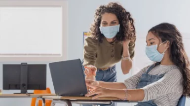 En lärare och en student bär masker och studerar en bärbar dator.