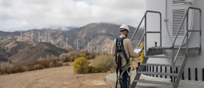 Mężczyzna w kasku stojący obok turbiny wiatrowej.