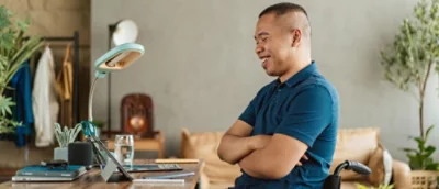 Un hombre sonriente con una camiseta azul se sitúa en un escritorio con una tableta.
