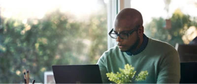 A man wearing glasses looking at a laptop.